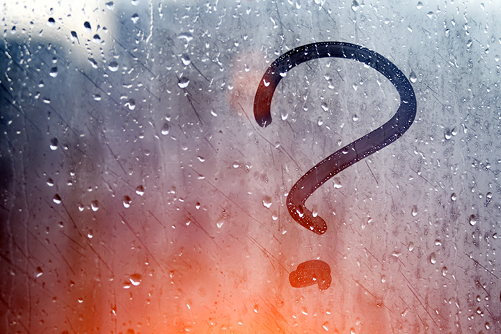 question mark drawn into rainy, misty window with subtle orange light in background